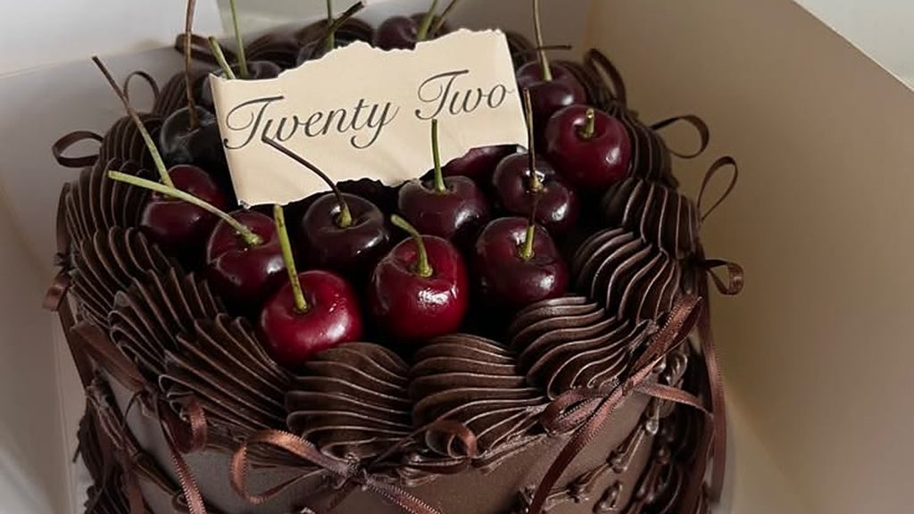 Chocolate cherry cake with fresh cherries in an open white box, whole stemmed dark cherries heaped inside a ring of piped swirls on ribbed dark frosting