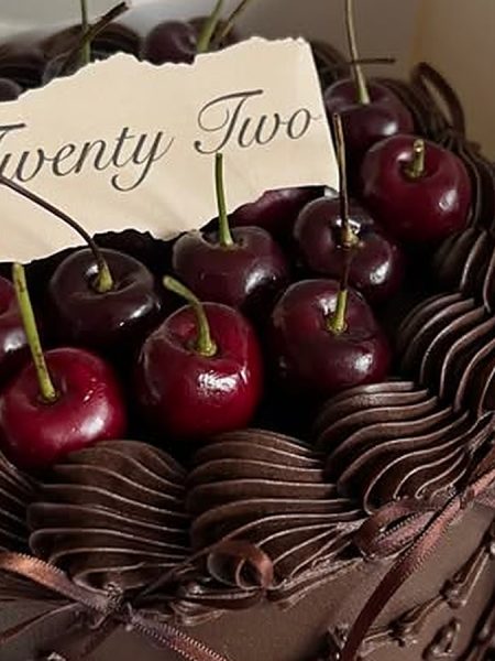 Chocolate cherry cake with fresh cherries in an open white box, whole stemmed dark cherries heaped inside a ring of piped swirls on ribbed dark frosting