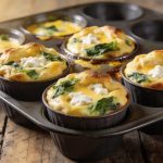 High protein egg muffins with cottage cheese: four golden tops risen above the cups of a dark muffin pan, white curds and green spinach on each.