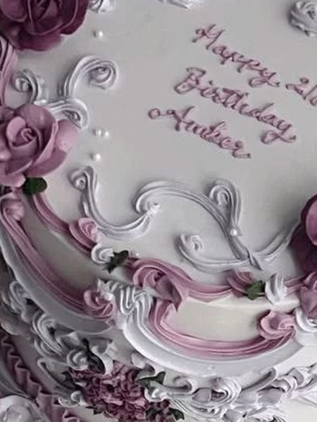 Vintage buttercream cake piped with white and pink scrollwork, draped swags and deep plum roses, with a birthday message written across the ivory top